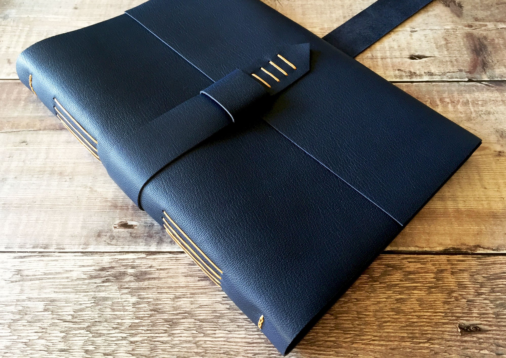 Leather Journal bound by hand in Navy Blue, with strap to close, A4 large against wood background.