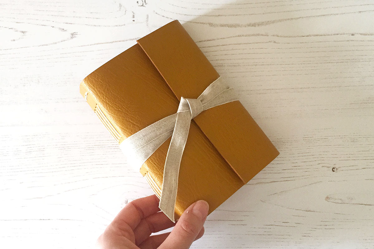 Hand holds A6 Journal or Sketchbook bound in Mustard Yellow leather with linen ribbon