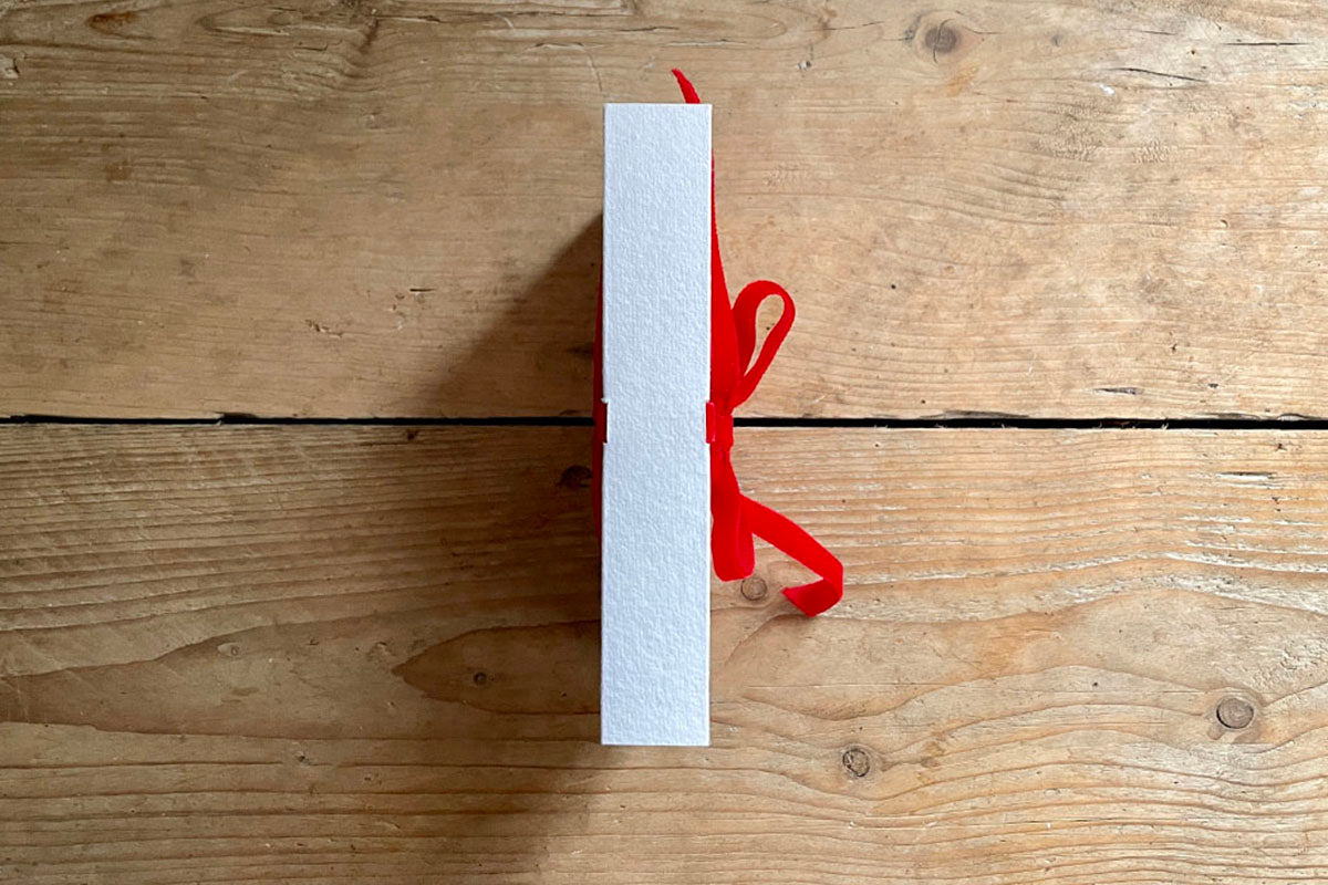Artist holds cotton rag sketchbook bound with handmade paper and a red velvet ribbon, its exposed spine binding faces the camera.