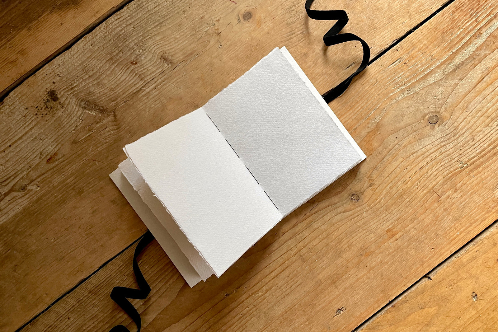 Lay flat sketchbook with 210gsm handmade cotton rag paper sized for wet and dry art work with black velvet ribbon.