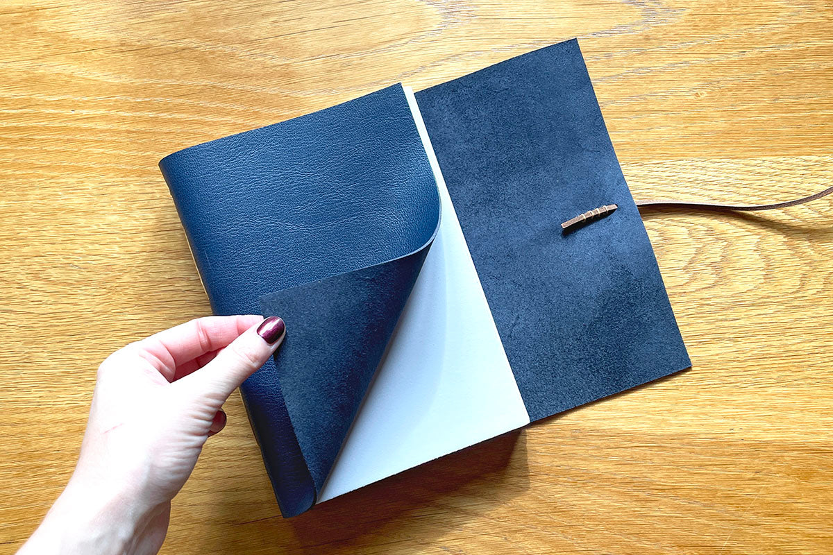 Hand turns softcover leather sketchbook to reveal cartridge paper pages with hand torn edges.