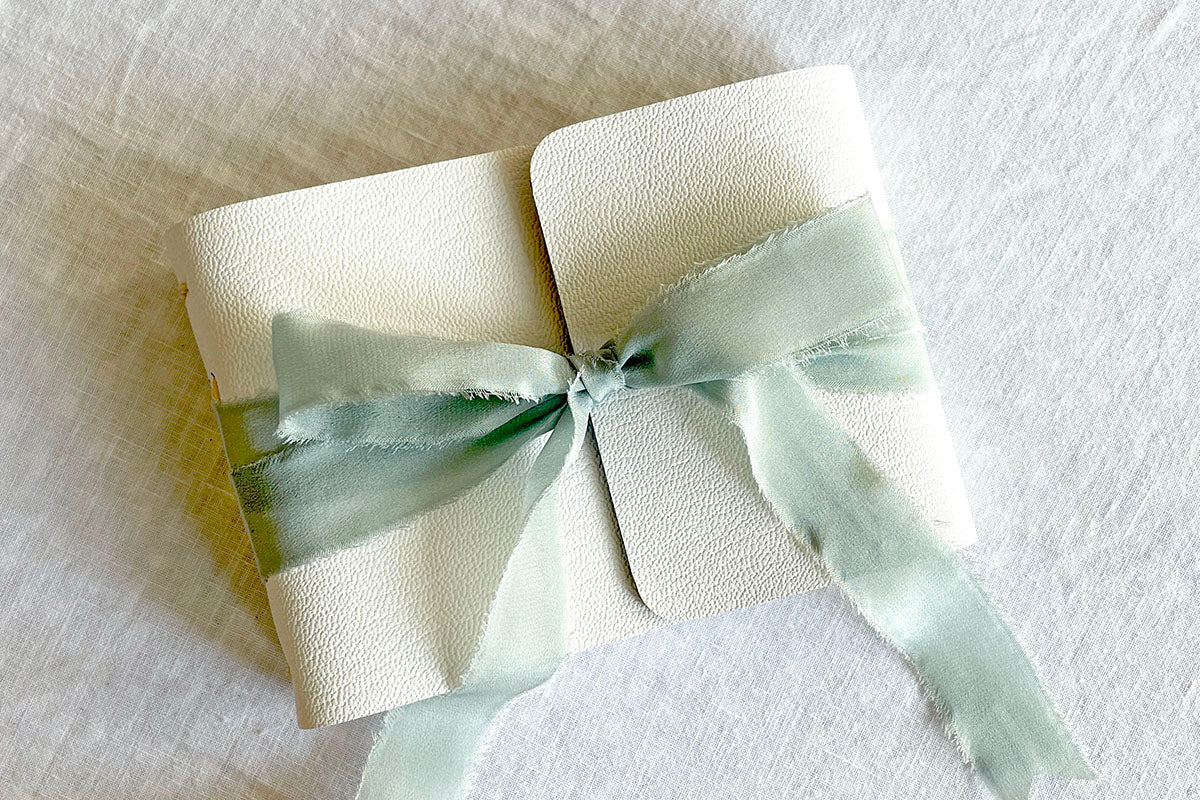 Sea Mist raw edge silk ribbon features on this A6 small white leather guest book