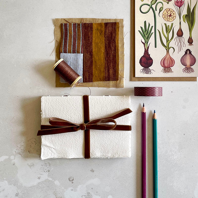 Handmade cotton rag sketchbook with Brown velvet ribbon and art materials including watercolour pencils,textiles, and botanical themed stationery.