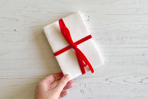 Artist holds corner of an A6 portrait handmade Cotton Rag Sketchbook tied with a Red Velvet Ribbon