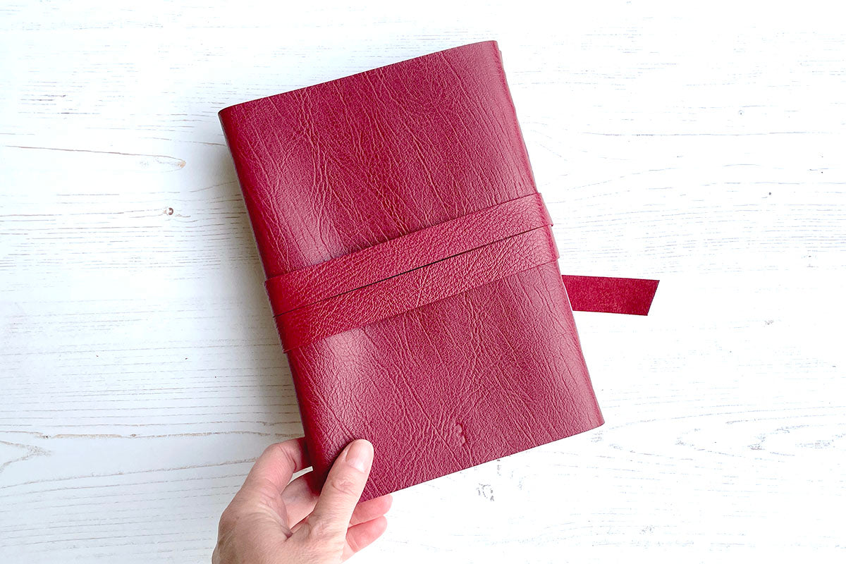 Back cover of A5 portrait Crimson Artist's Sketchbook featuring discrete bookbinder's studio mark debossed towards the tail, and natural grain leather.