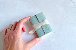 Bookbinder holds a Miniature Journal bound in Duck Egg leather with linen ribbon tied around its centre to keep it closed.