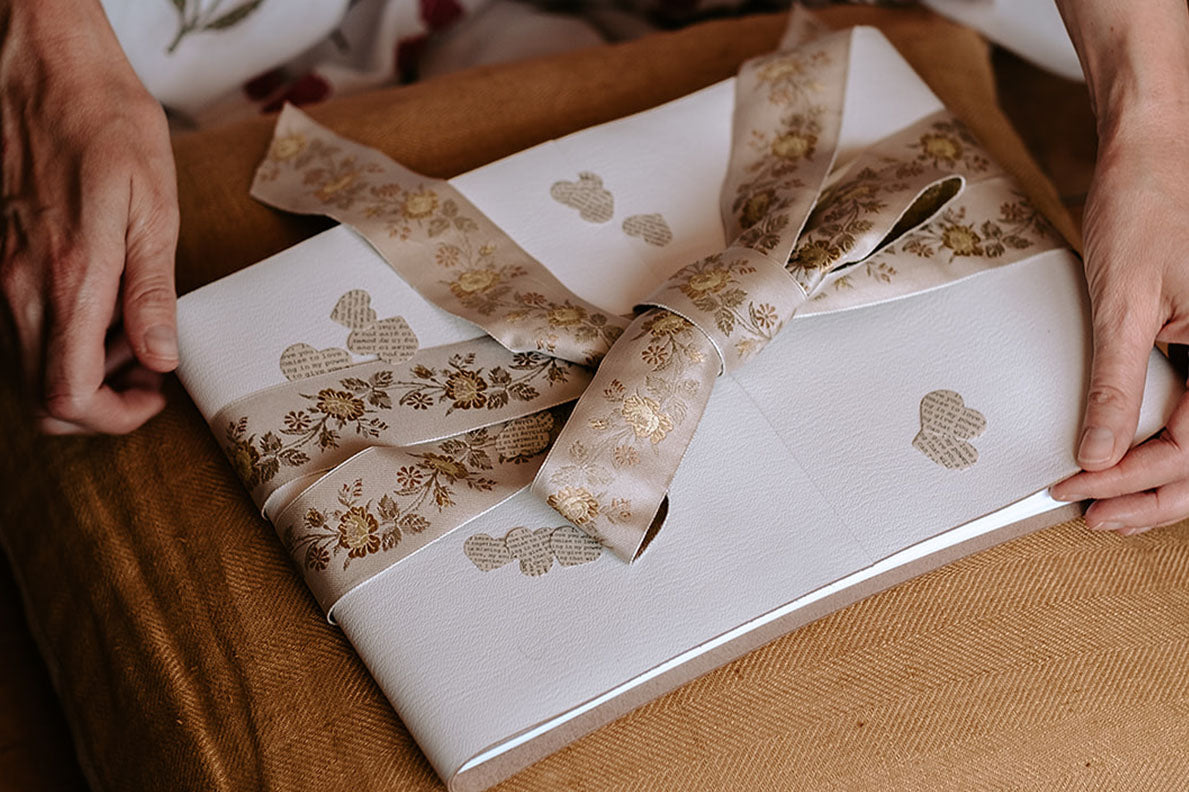 Luxurious jacquard floral silk ribbon keeps this white leather wedding guest book closed when not in use