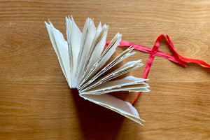 Cotton rag sketchbook bound with red silk ribbon, stands open on natural wood surface to show handmade deckle edge pages.