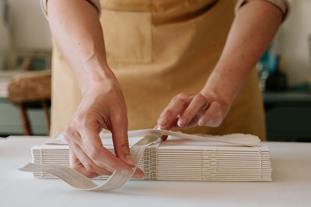 Handmade cotton rag sketchbook with exposed spine bound by artisan bookbinder Susan Green, who ties its linen ribbon. 