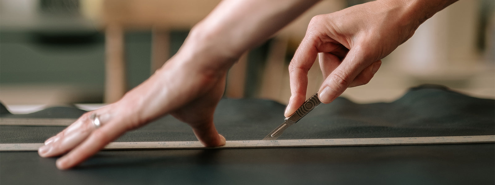 Bookbinder cuts leather for handmade book using scalpel and straight edge.