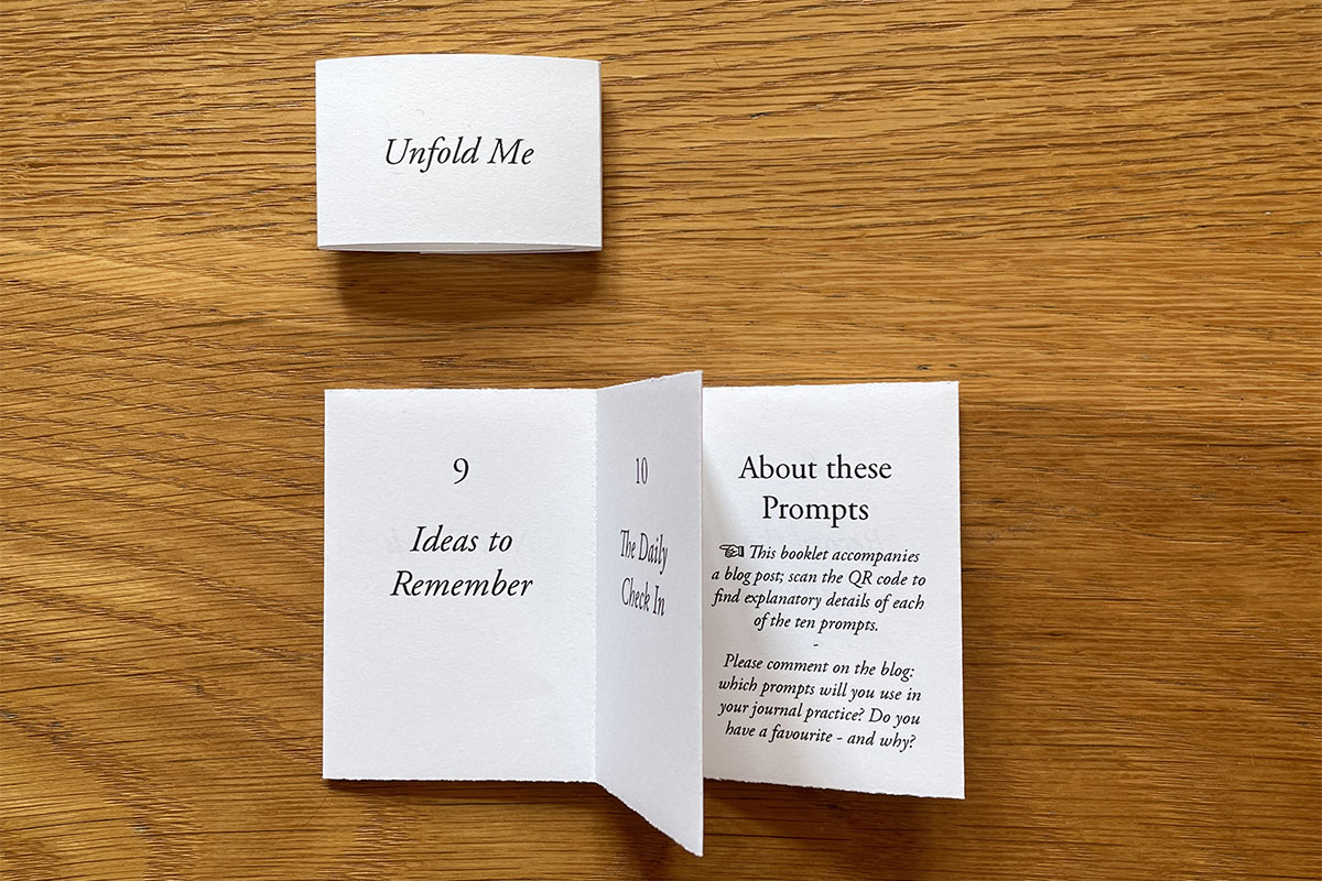 Artist's Book of journaling prompts with open folded Leporello pages and belly band