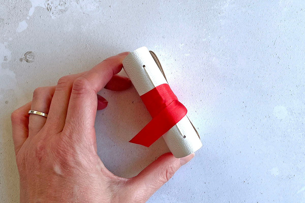 Miniature Journal bound in white leather with red silk, held by bookbinder.