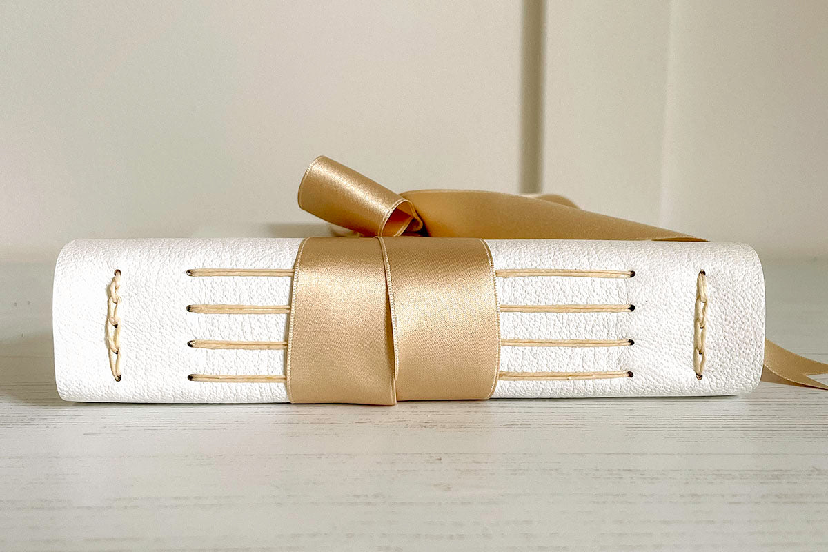 Lay flat exposed spine binding of leather wedding guest book bound by hand in white leather and natural silk