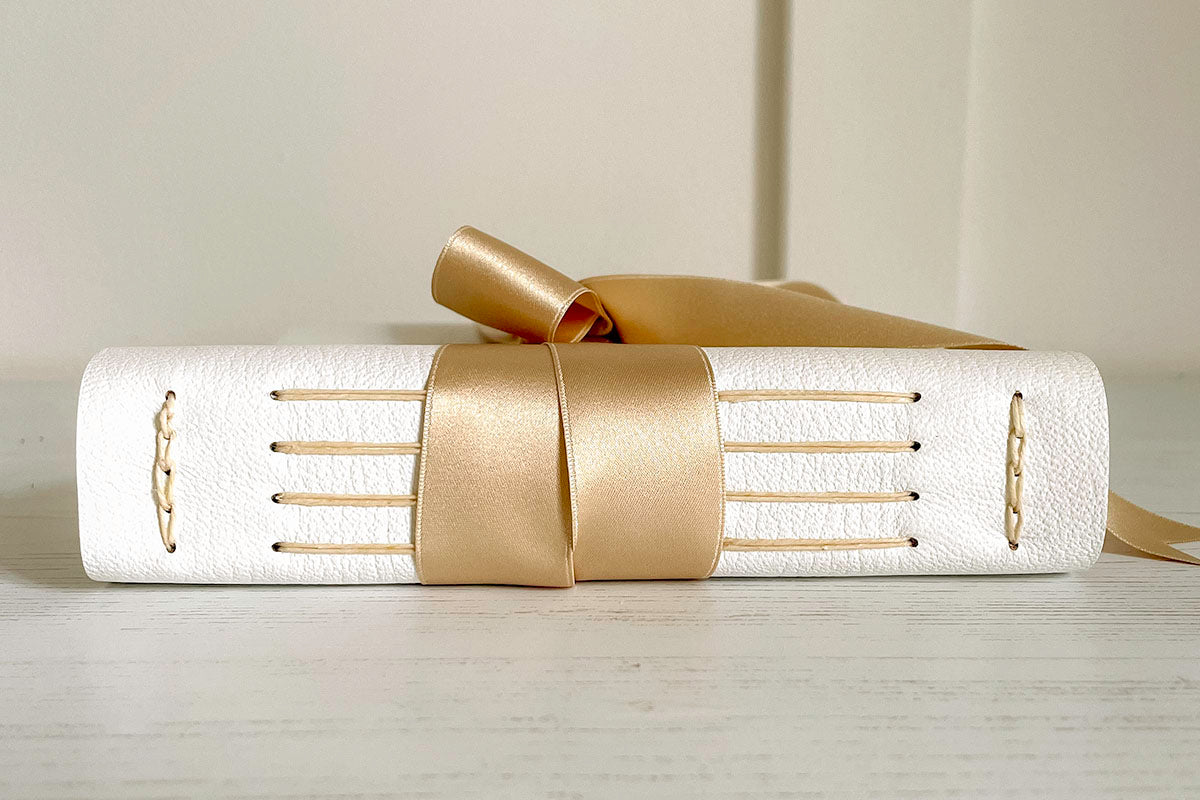 Lay flat Wedding Guest Book bound in white leather and natural silk ribbon, exposed spine.