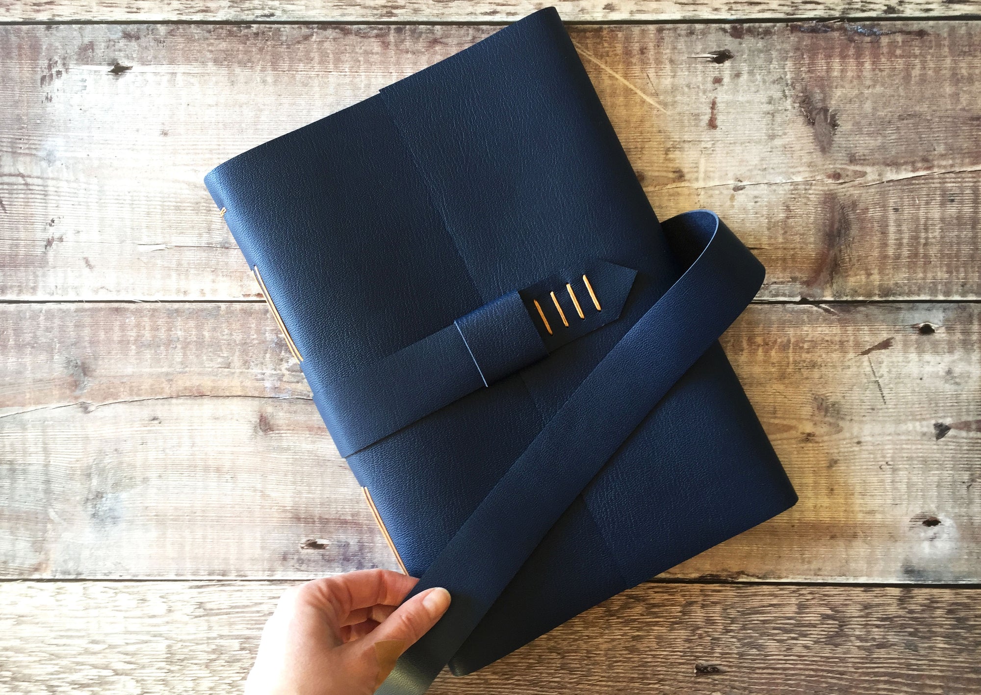 Leather Journal bound by hand in Navy Blue, with strap to close, A4 large against wood background.