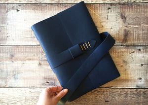 Leather Journal bound by hand in Navy Blue, with strap to close, A4 large against wood background.