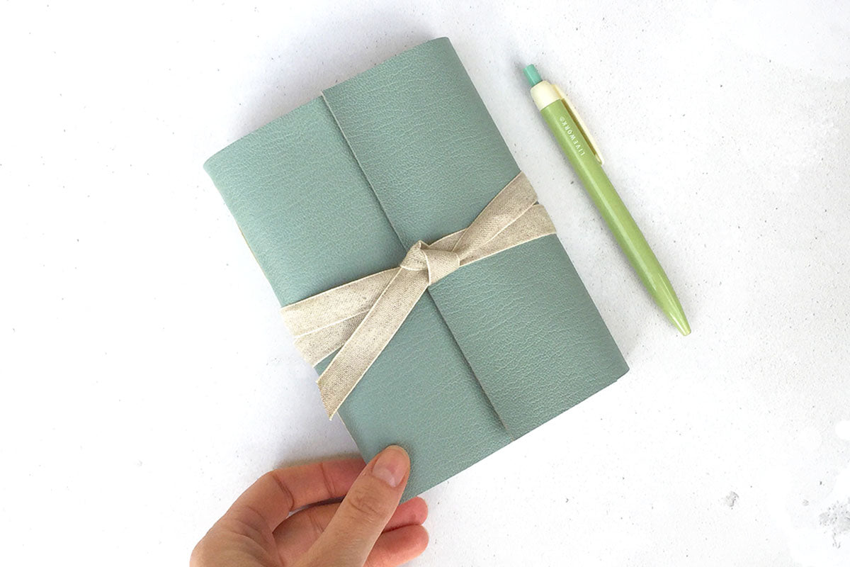 A6 Leather Sketchbook / Journal in Duck Egg with natural linen ribbon, a pen shows size.