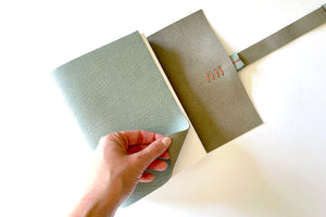 Hand turns cover of A5 portrait softcover leather bound Memory Book / Scrapbook in Duck Egg and Coral.